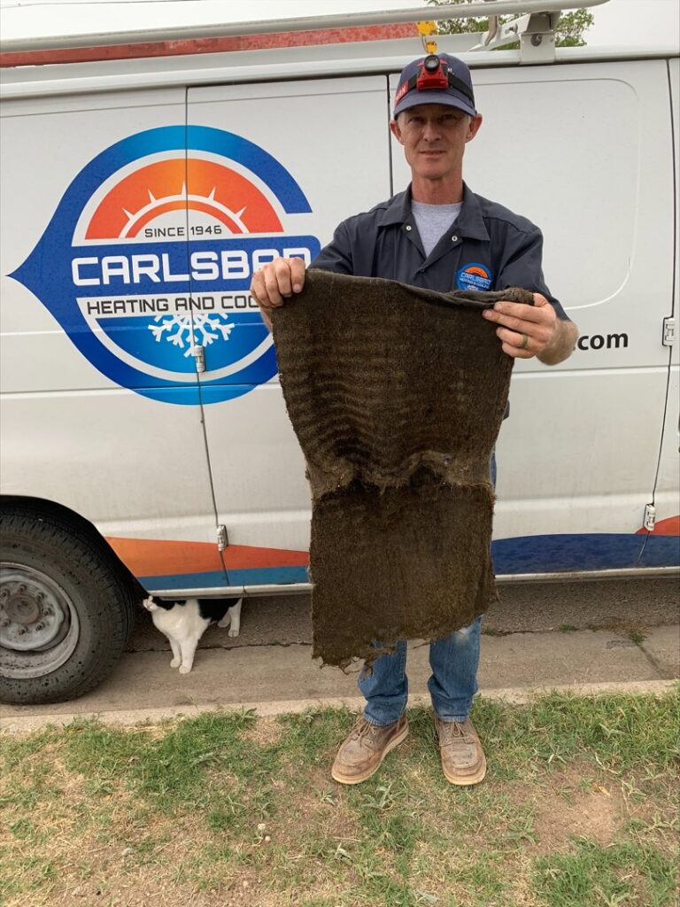 An HVAC technician holding up a very dirty air filter or insulation, demonstrating the need for maintenance from Carlsbad Heating & Cooling in Carlsbad, NM.