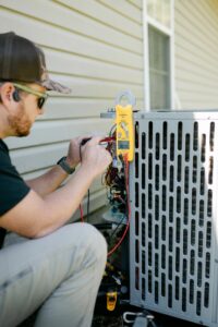 An HVAC technician using a multimeter to test an outdoor air conditioning unit for Wingman Heating + Cooling in Auburn, AL.