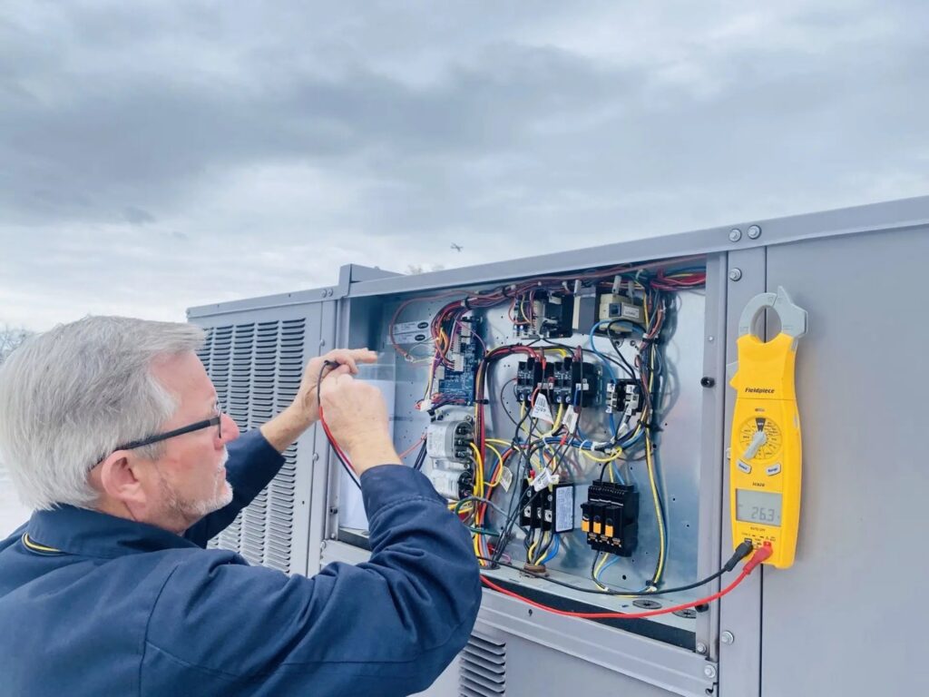 An HVAC technician testing a commercial rooftop unit's control panel with a multimeter for Air Works of Alabama LLC in Mobile, AL.