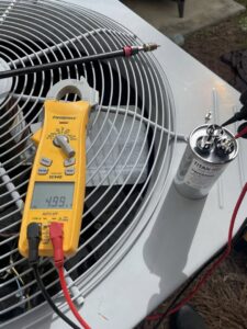 An HVAC technician using a multimeter to test a capacitor on an outdoor condenser unit by Arctic Desert Cooling & Heating in Concord, NC