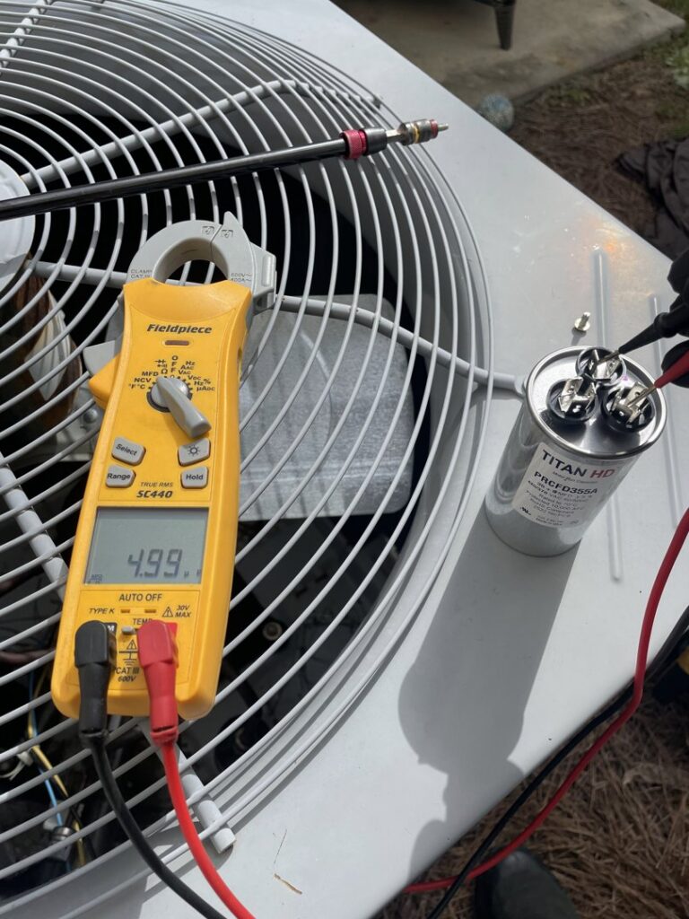 An HVAC technician using a multimeter to test a capacitor on an outdoor condenser unit by Arctic Desert Cooling & Heating in Concord, NC
