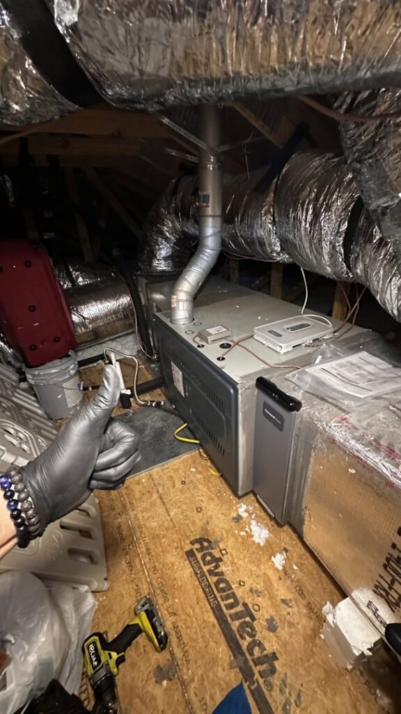 An HVAC technician giving a thumbs up next to a furnace and ductwork in an attic by Bree HVAC Contractor in Cedar Park, TX.