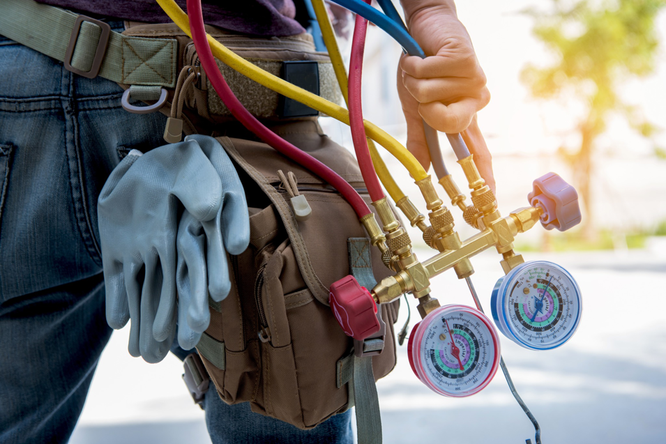An HVAC technician holding manifold gauges and tools, ready for service by Basic HVAC in Indianapolis, IN.