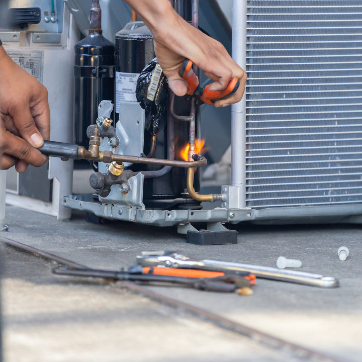 An HVAC technician using a torch to work on a component of an outdoor air conditioning unit for Eleven Heating and Cooling in Birmingham, AL.