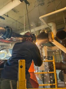 An HVAC technician welding pipes during an installation by Detroit Metro Mechanical, Inc. in Harrison Township, MI.