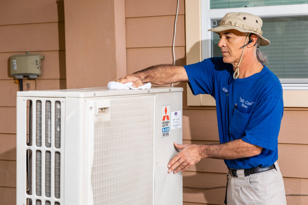An HVAC technician from Mr. Cool HVAC wiping down an outdoor Mitsubishi Electric air conditioning unit in Cypress, TX.