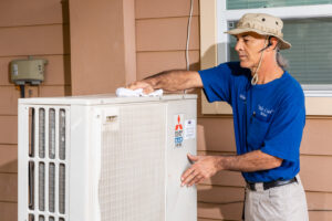 An HVAC technician from Mr. Cool HVAC wiping down an outdoor Mitsubishi Electric air conditioning unit in Cypress, TX.