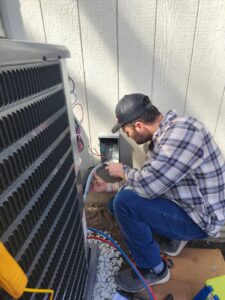 An HVAC technician connecting electrical wiring to an outdoor air conditioning unit for Dad's Heating and Cooling in Blue Springs, MO.