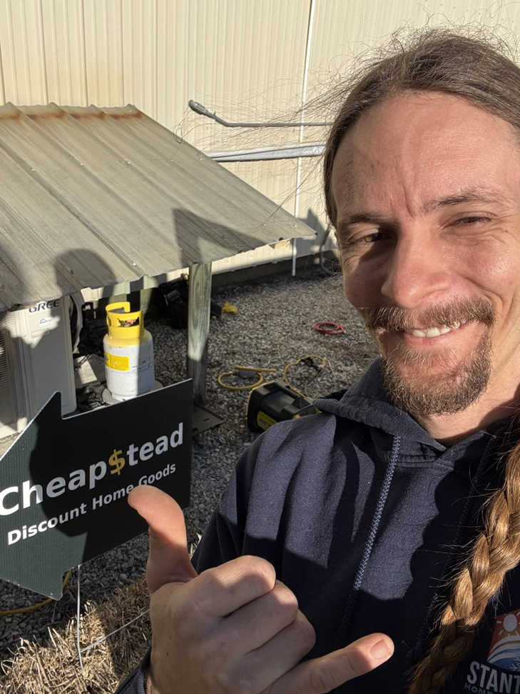 An HVAC technician with an outdoor AC unit and refrigerant tank at a job site for Stanton Home Comfort in Fordland, MO.