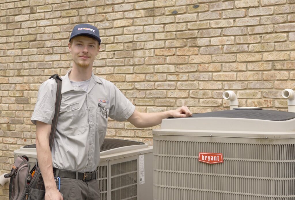 A FLAME Heating, Cooling, Plumbing & Electrical technician standing next to Bryant AC units in Warren, MI.