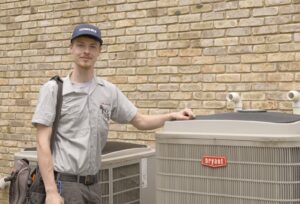 A FLAME Heating, Cooling, Plumbing & Electrical technician standing next to Bryant AC units in Warren, MI.