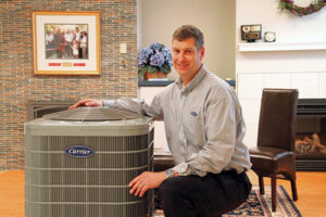 An HVAC technician kneeling beside a Carrier outdoor air conditioning unit for Hawn Heating and Air Conditioning in Rochester, NY.