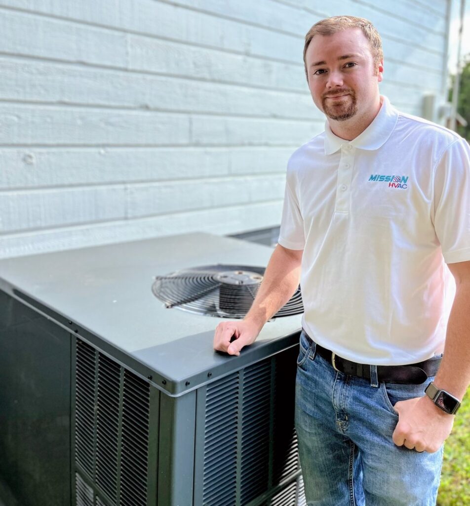 A Mission HVAC technician standing proudly next to a residential outdoor condenser unit in Huntsville, AL.