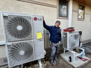 An HVAC technician stands proudly next to two newly installed LG heat pump units by Just Heat Pumps in Denver, CO.