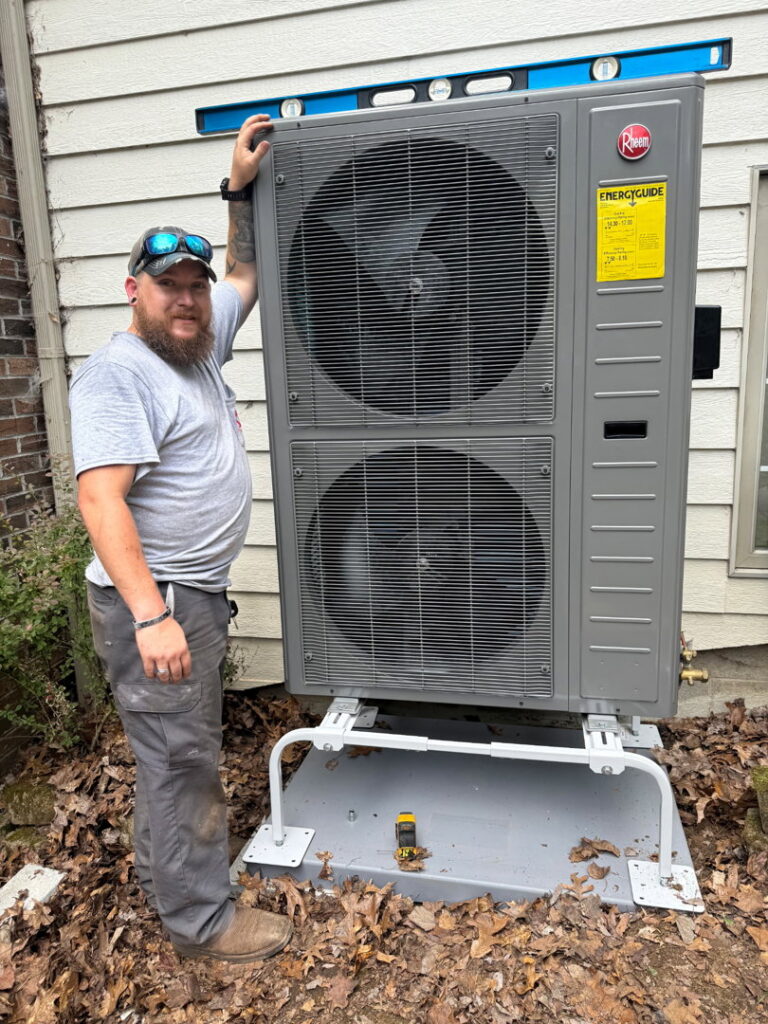 An HVAC technician standing proudly next to a newly installed outdoor heat pump unit for Empire Heating & Air Conditioning in Decatur, GA