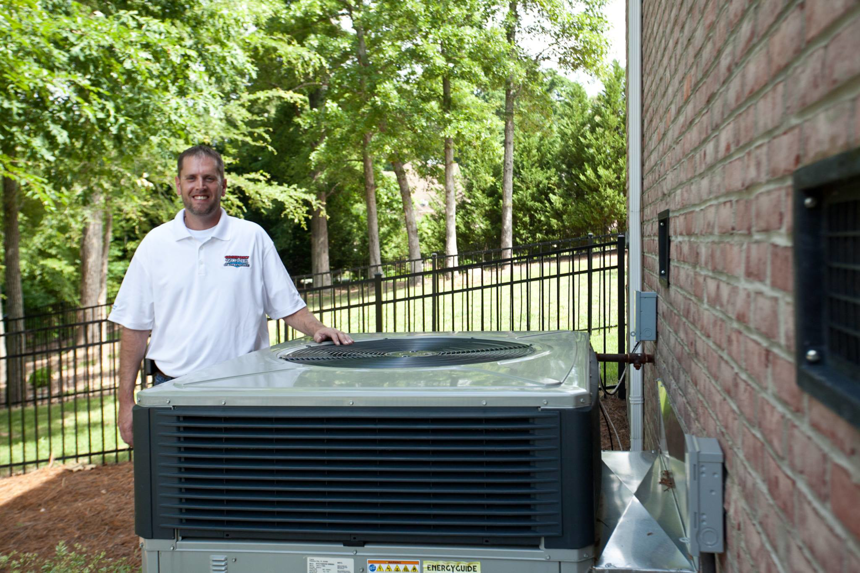 An HVAC technician standing proudly next to an outdoor air conditioning unit at Comfort Zone of the Carolinas in Rock Hill, SC.