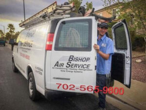 An HVAC technician from Bishop Air Service smiling next to a branded service van in Henderson, NV.