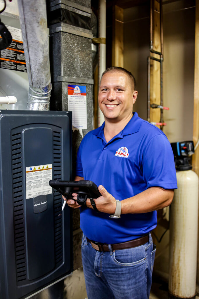An HVAC technician from Family Heating & Air Conditioning holding a tablet next to a furnace unit in Indianapolis, IN.