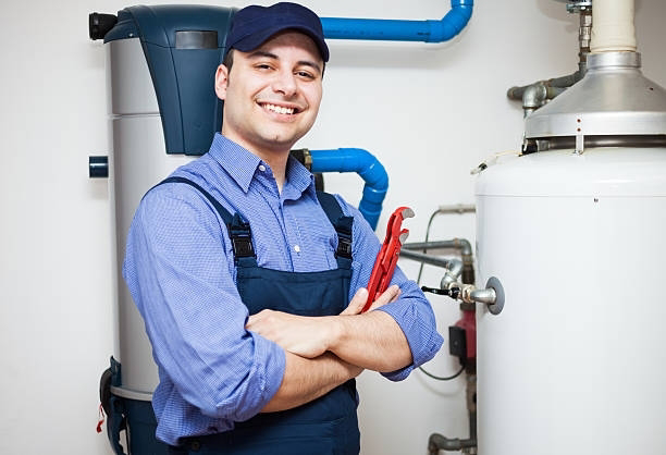 A smiling HVAC technician holding a wrench next to water heating equipment for Cleveland Air Comfort in Solon, OH.