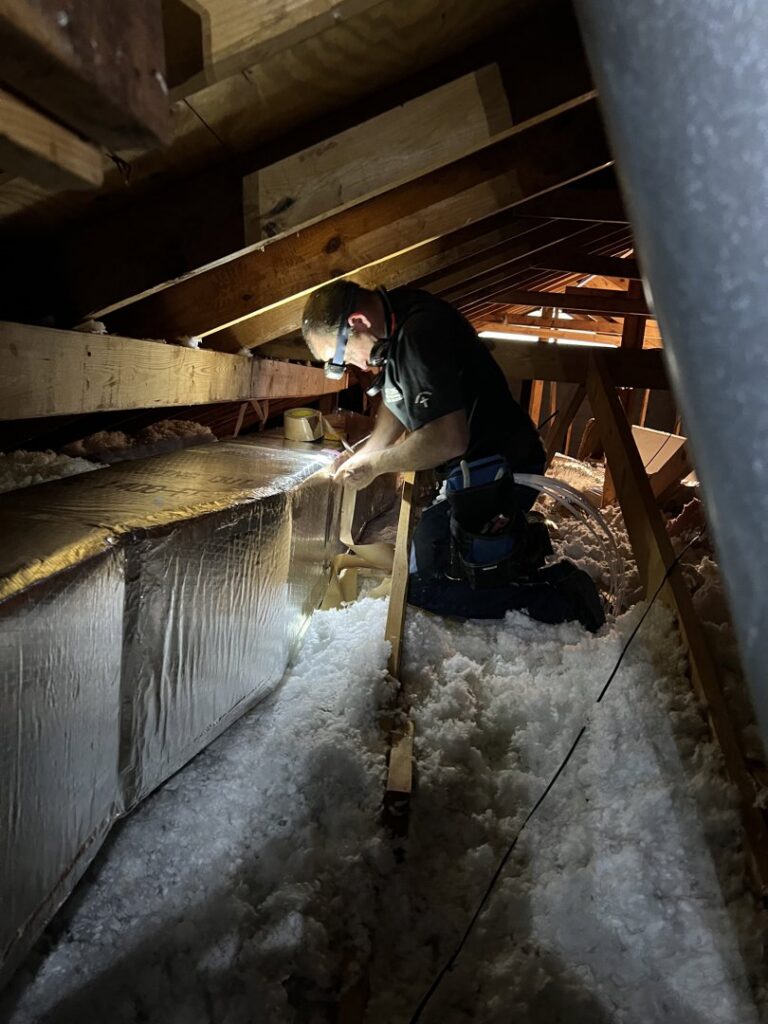 An HVAC technician working on ductwork in an attic for Fields Cooling Heating & Refrigeration in Foley, AL.