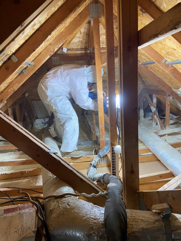 A Service Legends HVAC technician in a protective suit working on insulation and ductwork in an attic in Des Moines, IA.