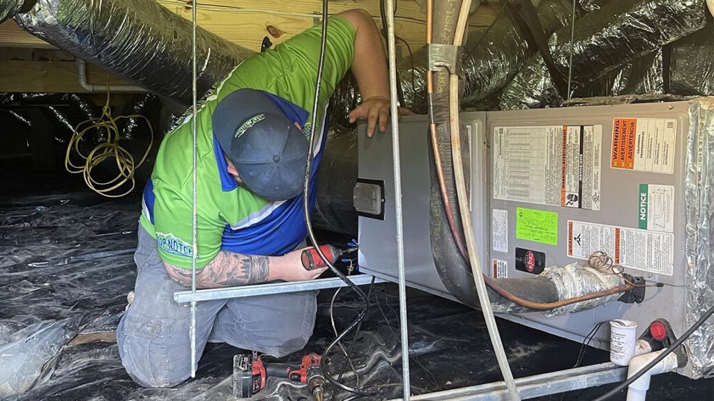 An HVAC technician from Top Notch Heating and Air Conditioning working on an indoor unit in a crawl space in Bowling Green, KY.