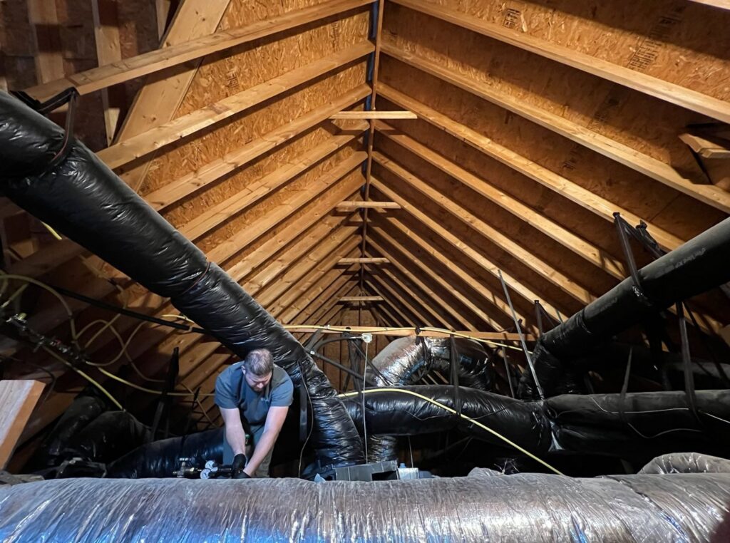 An HVAC technician working on ductwork installation in an attic for Sizemore Heating & Air, LLC in Chapel Hill, NC