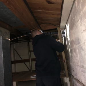An HVAC technician working on ductwork and pipes in a basement for SFC Heating and A/C, LLC in Alexandria, VA.