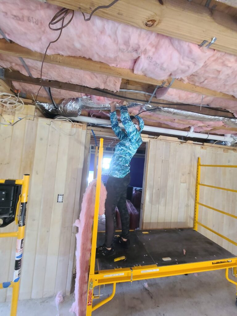 An HVAC technician working on wiring and insulation in an exposed ceiling during an installation by Rivertech Heating & Air Conditioning in Chattanooga, TN.