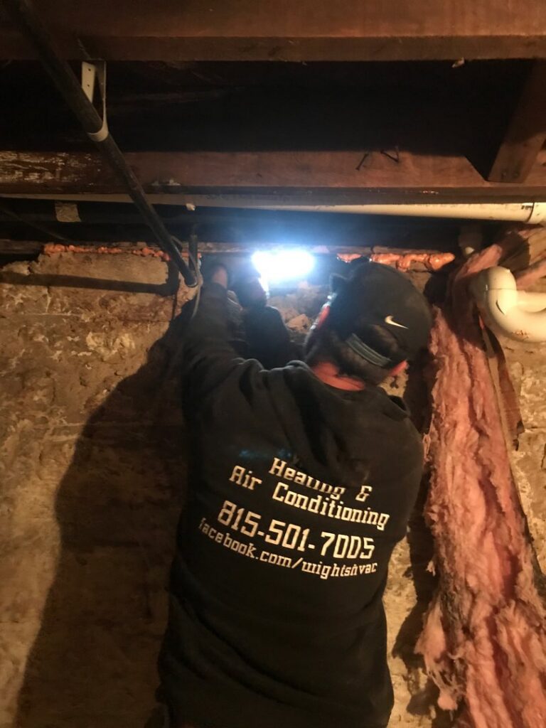 An HVAC technician from Wight's Heating & Air Conditioning working on ductwork in a crawlspace in Rockford, IL
