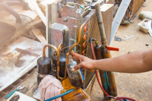 An HVAC technician working on an open AC compressor unit with tools and refrigerant bottles at Integrity Airworks in Hoover, AL.