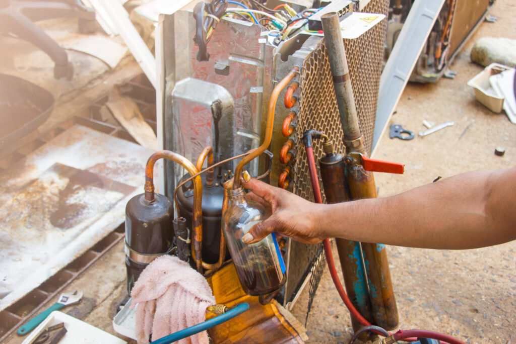 An HVAC technician working on an open AC compressor unit with tools and refrigerant bottles at Integrity Airworks in Hoover, AL.