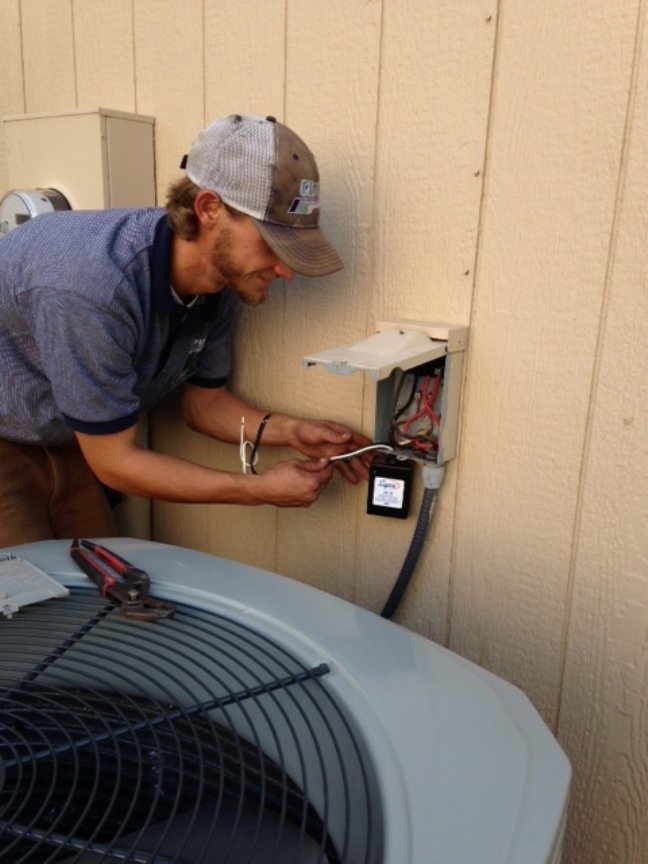 An HVAC technician performing service on an outdoor AC unit for Cloud Heating & Air Conditioning in Lawrence, KS.