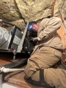 An HVAC technician working on an air handler in an attic for A/C Valley, LLC in Tempe, AZ.