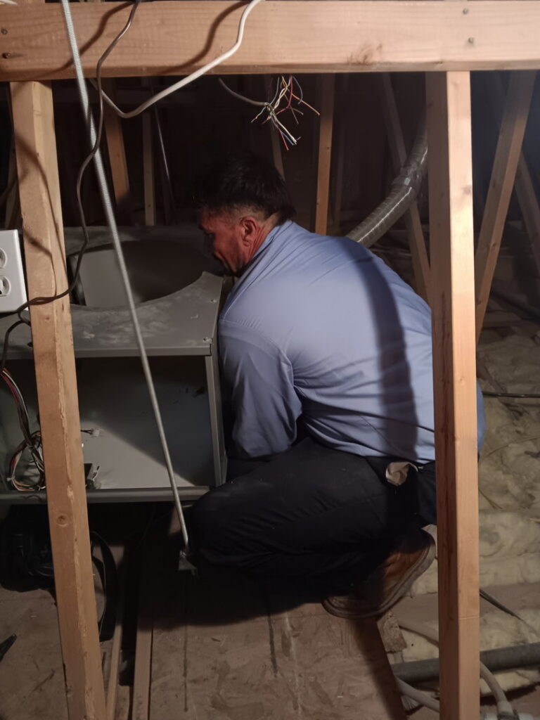 An HVAC technician working on an air handler unit in an attic for Bishop Air Service in Henderson, NV.