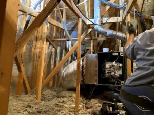 An HVAC technician working on an air handler and ductwork in an attic for Rebel Refrigeration in Las Vegas, NV.