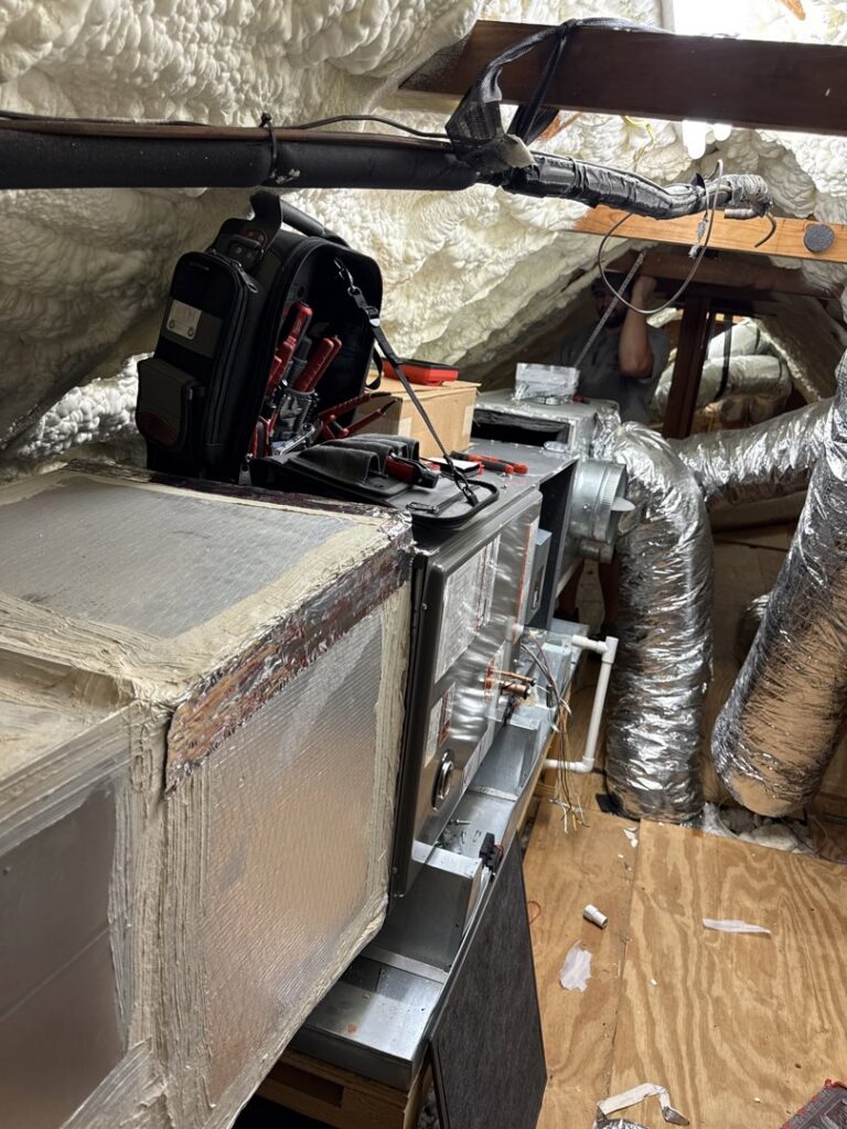 An HVAC technician working on an air handler unit and ductwork in an attic for Emergency Air in Chandler, AZ.