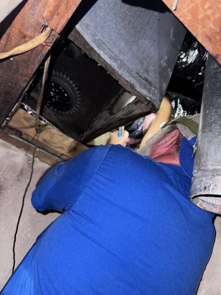 An ARKLA AIR LLC technician working on ductwork in a tight attic space, performing an HVAC repair or installation in Springhill, LA.