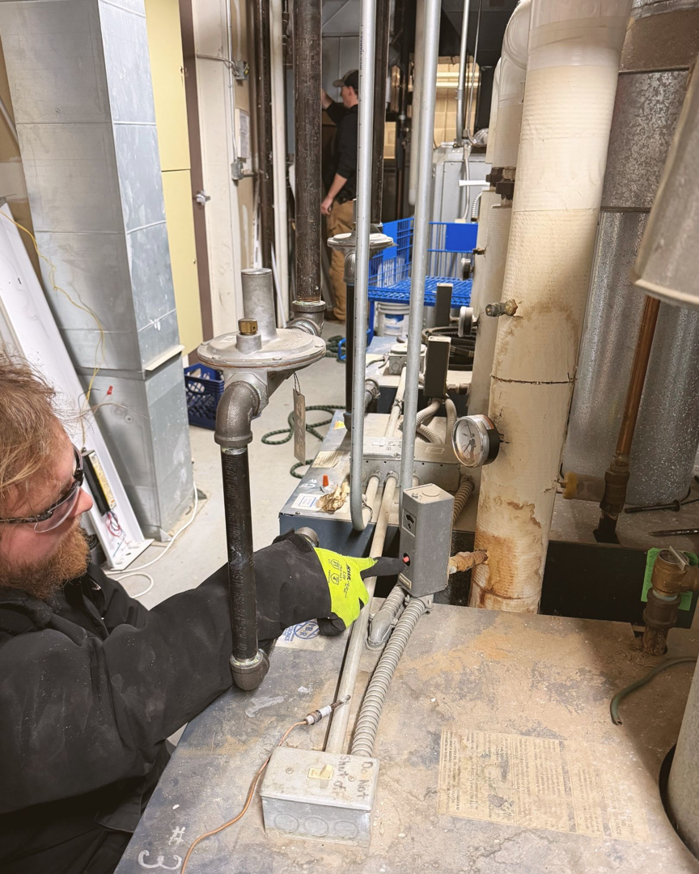 An HVAC technician performing work on boiler pipes and controls in a utility room for Climate Systems, Inc. in Sioux Falls, SD.