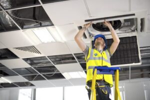 An HVAC technician from HVAC Philly on a ladder working on a ceiling-mounted commercial air conditioning unit in Feasterville, PA.
