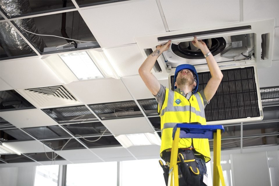 An HVAC technician from HVAC Philly on a ladder working on a ceiling-mounted commercial air conditioning unit in Feasterville, PA.