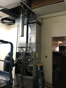 An HVAC technician working on a commercial unit with exposed components and ductwork by Epic Heating & Cooling in Wichita, KS.