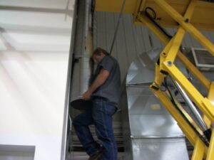 An Action Mechanical LLC technician on a scissor lift working on ductwork in a commercial building in Eau Claire, WI.