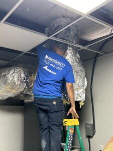 An Air Specialty Heating & Air Conditioning technician on a ladder working on exposed ductwork in Norfolk, VA.