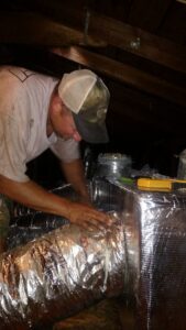 An HVAC technician working on ductwork installation or repair in an attic space for Get RiTe A/C & Heating in Madisonville, LA.