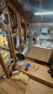 An HVAC technician working on ductwork and components in an attic for Pelican Heating and Air in Carlsbad, CA.