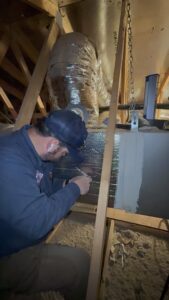 An HVAC technician from Rusty's Air Conditioning And Heating working on ductwork and an air handler in an attic in Mesa, AZ.