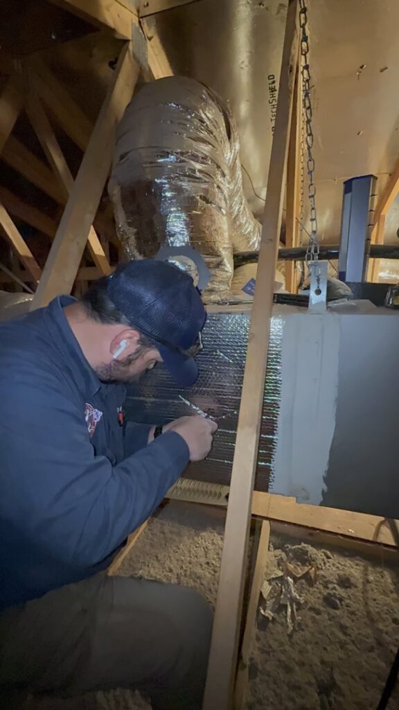 An HVAC technician from Rusty's Air Conditioning And Heating working on ductwork and an air handler in an attic in Mesa, AZ.