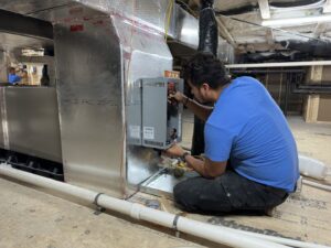 An HVAC technician working on a component attached to ductwork during an installation or service by Chad Byers - Edge Guys Heating & Cooling in Carmel, IN.