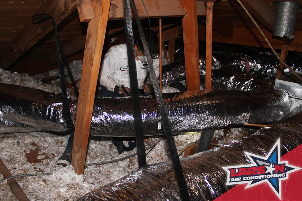 An HVAC technician working on ductwork and insulation in an attic for Larson Air Conditioning in Scottsdale, AZ